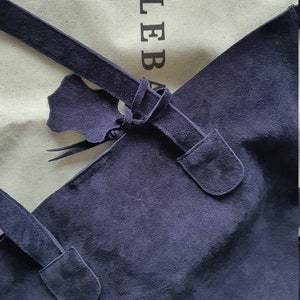 Op de afbeelding: Een marineblauwe su&egrave;de tote bag met een geknoopt banddetail. De tas heeft een rechthoekige vorm en een zachte textuur. De merknaam "MILEBA" is zichtbaar op de achtergrondstof.