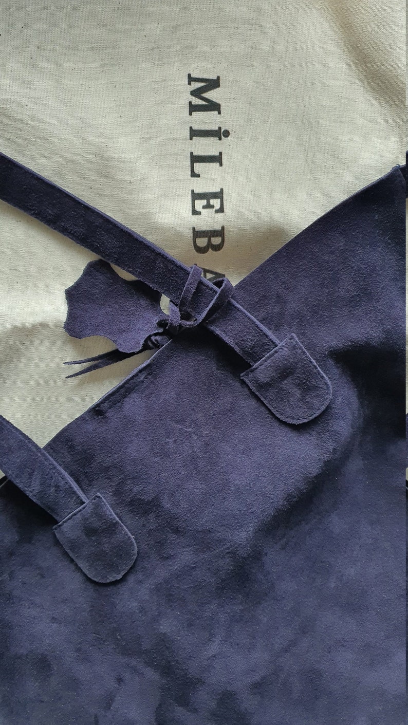 Op de afbeelding: Een marineblauwe su&egrave;de tote bag met een geknoopt banddetail. De tas heeft een rechthoekige vorm en een zachte textuur. De merknaam "MILEBA" is zichtbaar op de achtergrondstof.