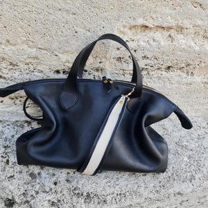 May include: A black leather tote bag with a white and black strap. The bag has a zipper closure and gold hardware.