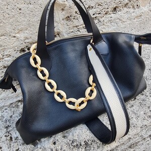 May include: Black leather tote bag with a white and black strap and a gold chain with cream-colored links.
