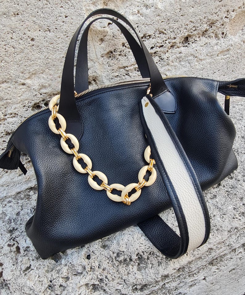 May include: Black leather tote bag with a white and black strap and a gold chain with cream-colored links.