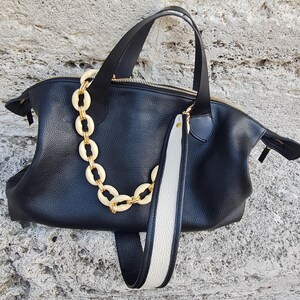 May include: A black leather tote bag with a white and black strap and a gold chain detail.