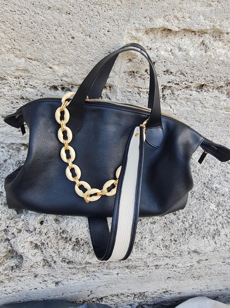 May include: A black leather tote bag with a white and black strap and a gold chain detail.