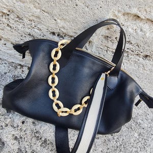 May include: Black leather tote bag with a white and black strap and a gold chain with cream-colored links.