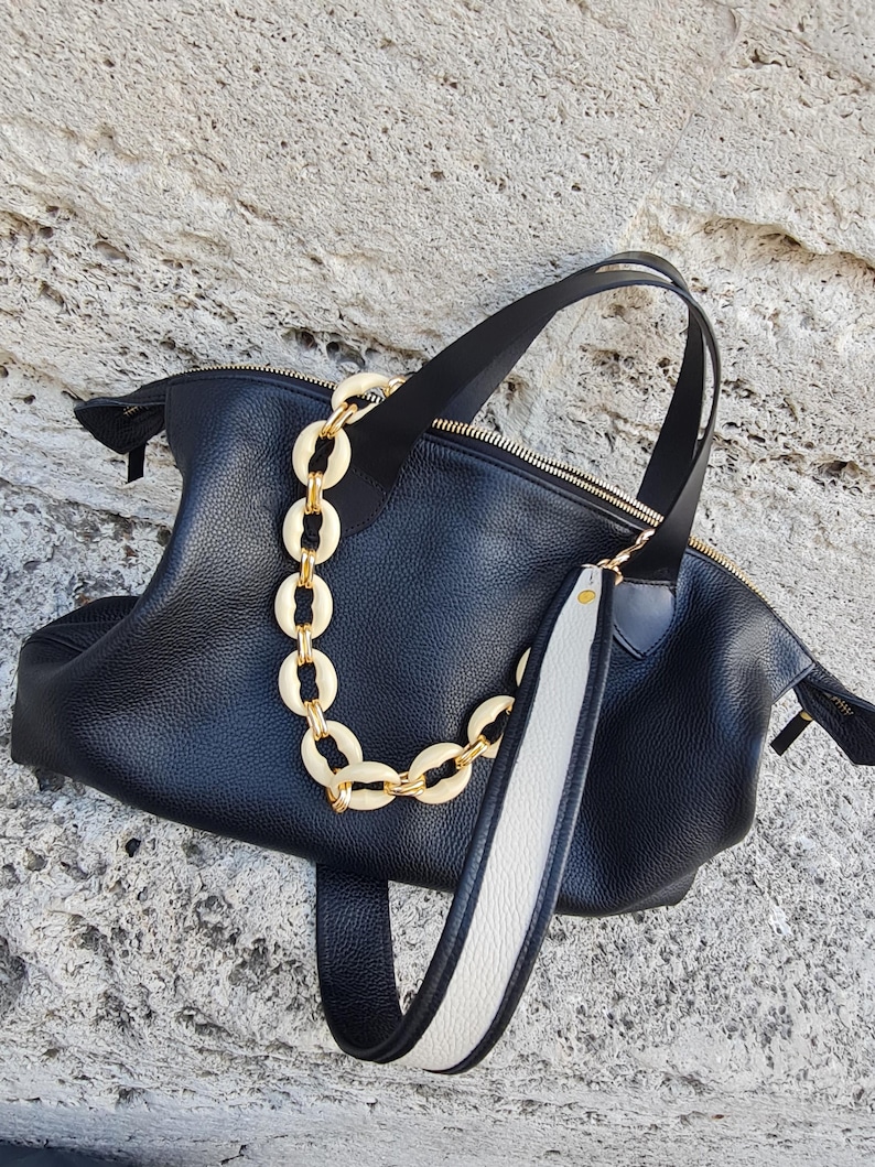 May include: Black leather tote bag with a white and black strap and a gold chain with cream-colored links.