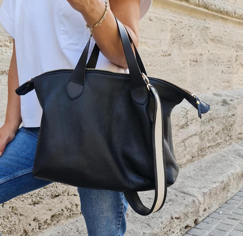 May include: A black leather tote bag with a white stripe on the strap. The bag has a zipper closure and a top handle.