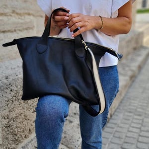May include: A black leather tote bag with a white stripe down the side. The bag has a top zipper closure and two top handles.