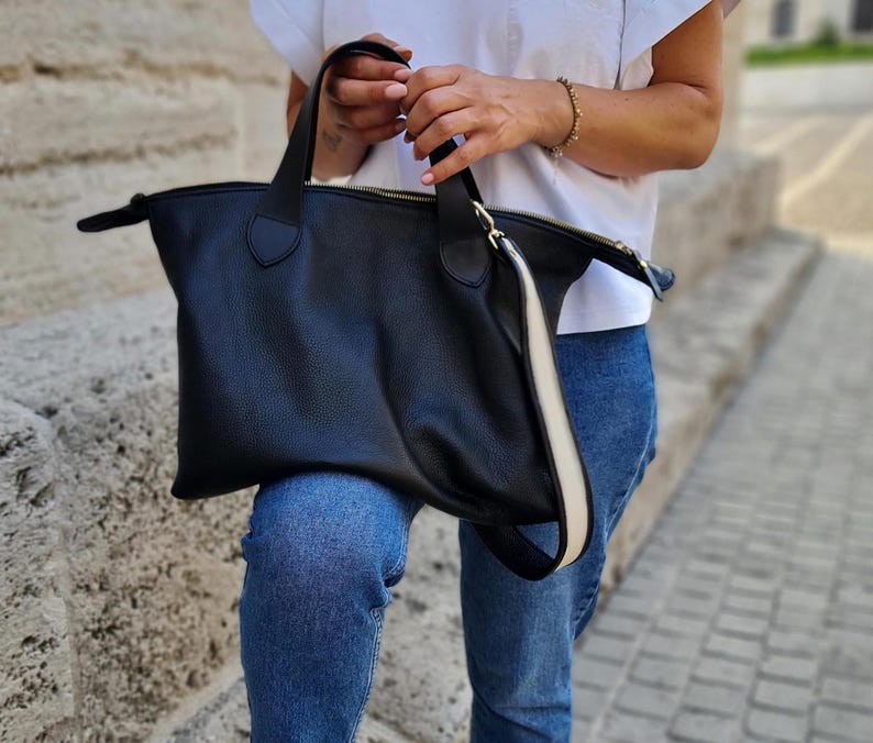 May include: A black leather tote bag with a white stripe down the side. The bag has a top zipper closure and two top handles.