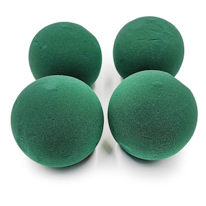 Op de afbeelding: Vier groene bloemschuimbollen op een witte achtergrond. De bollen zijn donkergroen en hebben een licht gestructureerd oppervlak. Ze worden gebruikt in de bloemsierkunst om bloemen te fixeren. Elke bol heeft een diameter van ongeveer 10 cm.