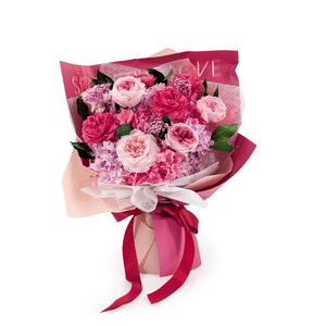 Op de afbeelding: Een boeket van geconserveerde bloemen in diverse tinten roze en magenta, bestaande uit rozen, hortensia's en kleine vulbloemen. Het arrangement is verpakt in gelaagd roze en donkerrood papier met de tekst SWEET LOVE en gestrikt met een rood lint.