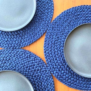 Könnte beinhalten: Drei blaue gewebte Tischsets mit grauen Keramiktellern darauf. Die Tischsets bestehen aus einem dicken, seilartigen Material und haben ein gewebtes Muster.