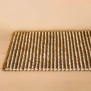 May include: A rectangular woven mat featuring alternating vertical stripes of natural brown jute rope and thin white cord. The texture is consistent throughout the piece, showcasing a repeating pattern of thick brown and narrow white fiber lines.