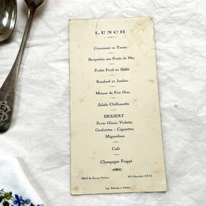 May include: A vintage rectangular paper menu from the Hotel de France in Poitiers, dated December 30, 1935. The off-white card features black printed text listing lunch and dessert items, including Consommé, Roasbeef, and Champagne Frappé.