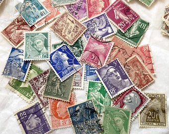 Op de afbeelding: Een verzameling vintage postzegels in verschillende kleuren, waaronder blauw, groen, rood en paars. De postzegels tonen portretten, illustraties en tekst, met zichtbare denominaties. De postzegels zijn gerangschikt op een wit oppervlak.