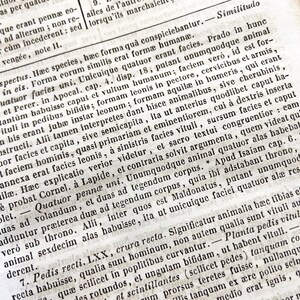 May include: A close-up of an open book page with Latin text. The page is aged, with visible wear and tear, and the text is densely packed in a classic serif font. The paper has a warm, off-white tone, suggesting age.