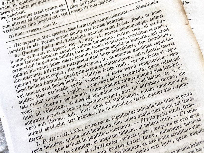 May include: A close-up of an open book page with Latin text. The page is aged, with visible wear and tear, and the text is densely packed in a classic serif font. The paper has a warm, off-white tone, suggesting age.