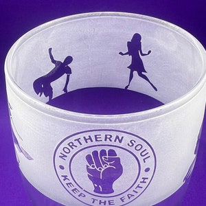 May include: A clear glass tumbler with a frosted design. The design features a purple silhouette of a fist with the words "Northern Soul Keep The Faith" around it.