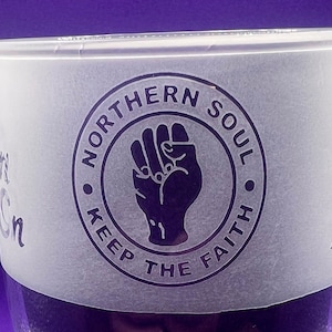 May include: A frosted glass pint glass with a white sticker featuring a black and white logo that says "Northern Soul Keep The Faith" with a raised fist in the centre.
