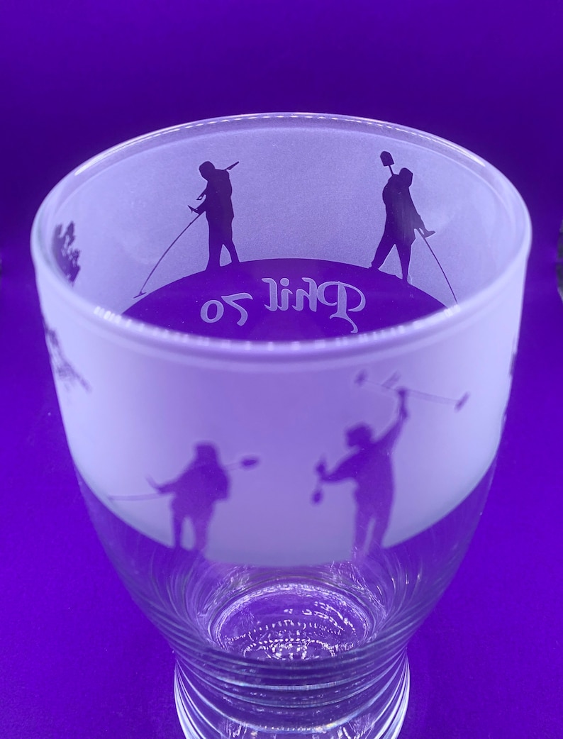 May include: A clear glass with a frosted upper section. The frosted area features silhouettes of golfers in action, with the word "Golf" in a stylized font. The glass has a flared shape and a detailed base.