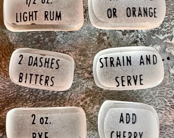 Pode incluir: Seis pedras retangulares de vidro fosco com texto impresso em preto. As pedras dizem: 1/2 oz. LIGHT RUM, ADD OLIVE OR ORANGE, 2 DASHES BITTERS, STRAIN AND SERVE, 2 oz. RYE e ADD CHERRY. Estas peças lisas e translúcidas têm bordas arredondadas.