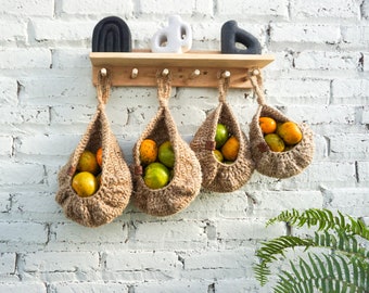 May include: Four hanging woven baskets filled with oranges and limes, hanging from a wooden shelf with hooks against a white brick wall.