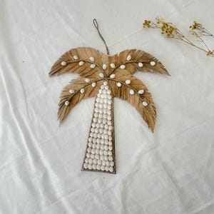 May include: A brown palm tree wall hanging made of woven palm leaves and decorated with white seashells.