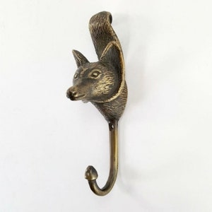 May include: A bronze fox head wall hook with a curved hook. The fox head is detailed with fur and has a realistic look.