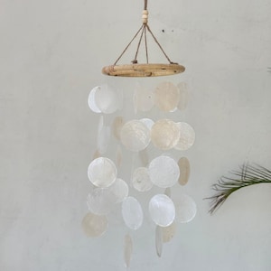 May include: A white seashell wind chime with a wooden ring at the top and multiple layers of shells hanging from it.