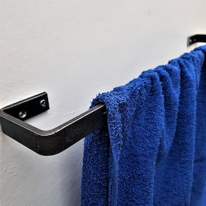 May include: A black metal towel rail mounted on a white wall with a blue towel hanging from it.