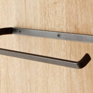 May include: Black metal towel bar with a curved design. The bar is mounted to a wooden wall.