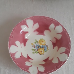 May include: A pink and white floral patterned bowl with a scalloped edge. The bowl features a central floral design with yellow and blue flowers. The bowl is likely made of ceramic or porcelain.