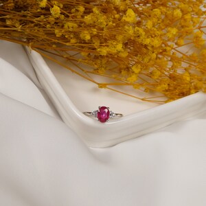Puede incluir: Un anillo de plata con una gran piedra de rub&iacute; ovalada y dos peque&ntilde;os acentos de diamantes.