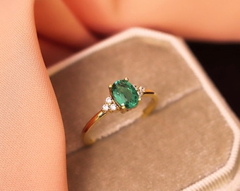 Peut inclure: Une bague en or ornée d'une pierre précieuse verte centrale de taille ovale, flanquée de trois petites pierres claires de chaque côté. L'anneau est fin et poli, présentant un sertissage à griffes classique qui maintient la pierre verte.