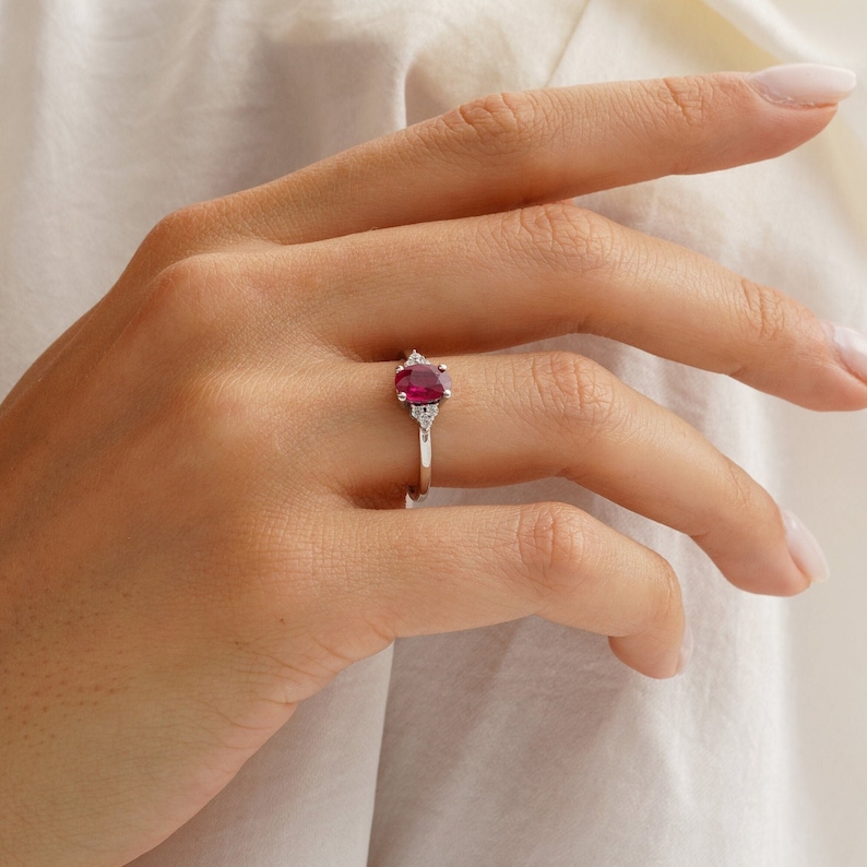 Puede incluir: Un anillo de plata con una piedra ovalada roja y dos piedras blancas m&aacute;s peque&ntilde;as en la banda.