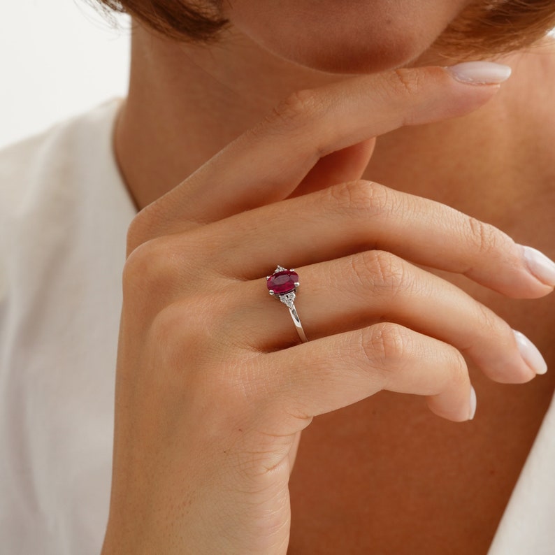 Puede incluir: Un anillo de plata con una piedra ovalada roja y dos piedras blancas m&aacute;s peque&ntilde;as en la banda.