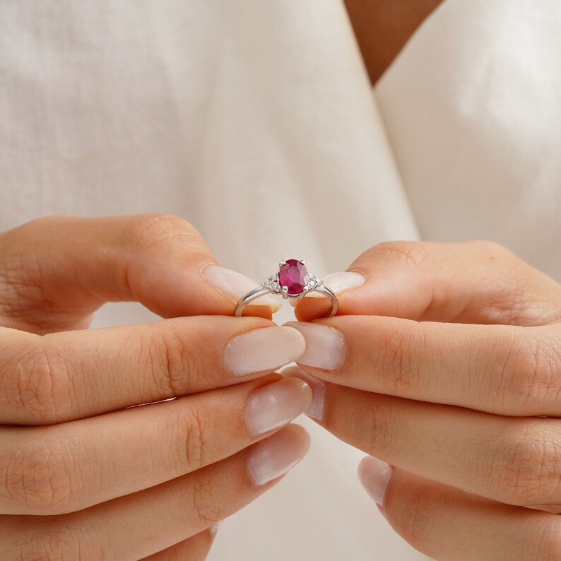 Puede incluir: Un anillo de plata con una gran piedra de rub&iacute; ovalada y dos peque&ntilde;os acentos de diamantes.