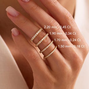 May include: Four gold eternity bands set with clear stones, displayed with text labels: 2.20 mm - 0.45 Ct, 1.90 mm - 0.34 Ct, 1.70 mm - 0.24 Ct, and 1.50 mm - 0.18 Ct. Each ring features a continuous row of small, sparkling stones in a gold setting.