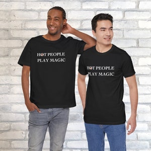May include: Two people wearing black t-shirts with white text that reads "Hot People Play Magic".