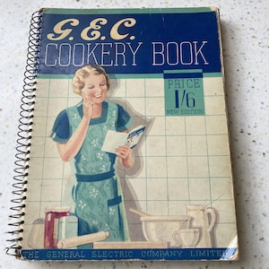May include: A vintage spiral-bound G.E.C. Cookery Book with a blue and cream cover. The illustration features a person in a green apron holding a small book, with kitchen items like a rolling pin and mixing bowl below. Text includes G.E.C. COOKERY BOOK.