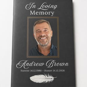Op de afbeelding: Een zwart uitvaartprogramma-boekje met de witte tekst In Loving Memory, een gecentreerde foto van een glimlachende man, de naam Andrew Brown, de data Sunrise 14.12.1986 - Sunset 14.12.2026 en een witte verengrafiek onderaan.