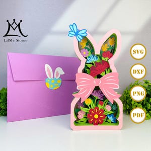 May include: A pink layered paper Easter bunny decoration with a pink bow, flowers, and a blue butterfly. A purple envelope with a bunny sticker is on the left. The image also includes SVG, DXF, PNG, and PDF icons.