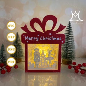 May include: A red Christmas-themed gift box with a bow, cut-out design, and the words "Merry Christmas." Inside, a lit scene depicts a nutcracker, ballerina, and Christmas tree. The image includes SVG, DXF, PNG, and PDF file type icons.