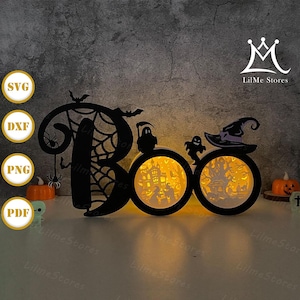 May include: A black Halloween-themed light-up decoration spelling "Boo". The "O"s feature illuminated cutouts of a haunted house and a spooky tree. Includes bats, spiders, a witch's hat, and ghosts. The text "LilMe Stores" is visible.