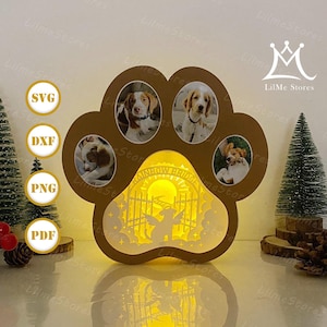 Op de afbeelding: Een bruine, pootvormige fotolijst met ruimte voor vier hondenfoto's. De lijst is verlicht en toont de tekst "Rainbow Bridge" en een engelen silhouet. De binnenverlichting zorgt voor een warme gloed.