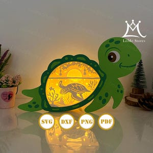 May include: A green turtle-shaped lamp with a detailed interior scene of a sunset over the ocean, featuring a turtle silhouette. The lamp has a decorative border and is lit from within, creating a warm glow. The image also includes the text "SVG, DXF, PNG, PDF".