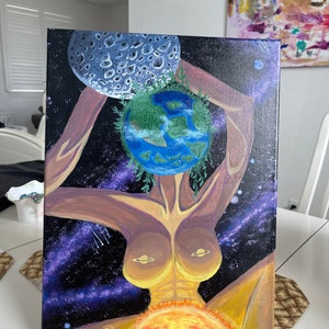Puede incluir: Una pintura que representa una figura femenina con un planeta Tierra como cabeza, sosteniendo una luna en su mano izquierda. La figura está rodeada de estrellas y un sol en la esquina inferior derecha. La pintura está firmada "MJ 2021" en la esquina inferior izquierda.