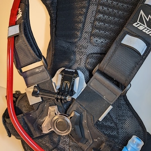 Pu&ograve; includere: Zaino di idratazione nero con un tubo di idratazione rosso e un beccuccio blu. Lo zaino ha un pannello posteriore in rete e un logo bianco e nero che dice "USWE". Lo zaino ha un supporto GoPro nero e argento.