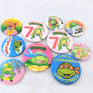 May include: A set of ten Teenage Mutant Ninja Turtles themed pinback buttons. The buttons are round and feature various images of the turtles, including their names, the number 7, and the phrase "Have a Cowabunga Christmas".