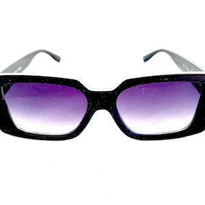 May include: Black square-shaped sunglasses with a white trim around the lenses. The lenses are a gradient purple color.