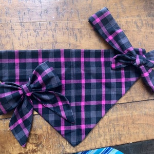 May include: A black and pink plaid bandana with a matching bow tie. The bandana is folded into a triangular shape and the bow tie is tied in a knot.